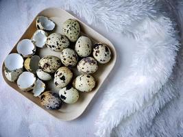 huevos de codorniz de codorniz, una colección de huevos de codorniz en un plato de madera con un fondo de manta de plumas blancas foto