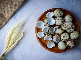 Quail eggs from quail, a collection of quail eggs on a wooden plate against a white wall background photo