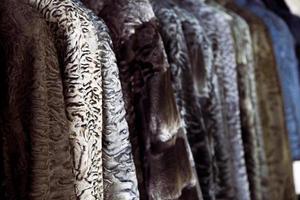 A close up of a fur coat from a natural fur of astrakhan of different colors  brown, gray and black, hang in one row in the store photo