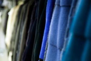 A close up of a fur coat from natural mink fur of different colors  gray, blue, green and black hanging in one row in the store photo