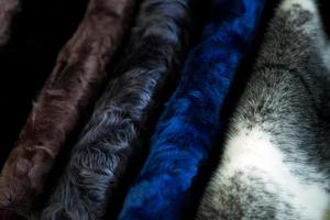A close up of a fur coat from a natural fur of astrakhan of different colors  brown, gray and black, hang in one row in the store photo