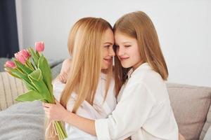Girls gives flowers. Young woman with her daughter is at home at daytime photo