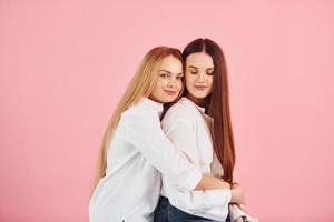 sobre fondo rosa. joven madre con su hija de pie en el estudio foto