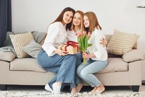 haciendo sorpresa con flores. joven madre con sus dos hijas en casa durante el día foto