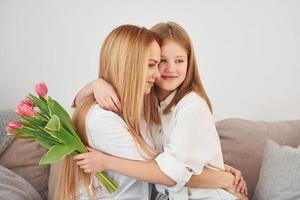 Girls gives flowers. Young woman with her daughter is at home at daytime photo