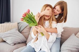 Embracing and giving flowers. Young mother with her daughter is at home at daytime photo