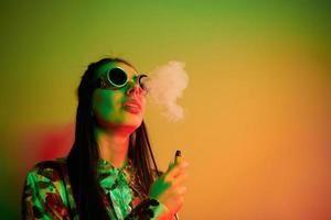 Smoking, activity. Fashionable young woman standing in the studio with neon light photo