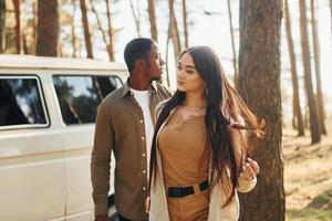 Bus is behind. Young couple is traveling in the forest at daytime together photo