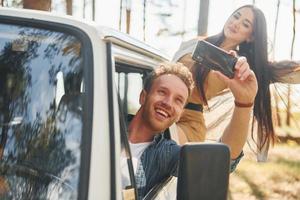 Making selfie. Young couple is traveling in the forest at daytime together photo