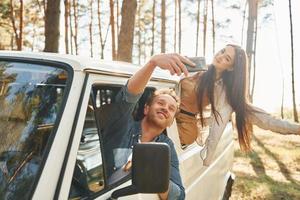 Making selfie. Young couple is traveling in the forest at daytime together photo