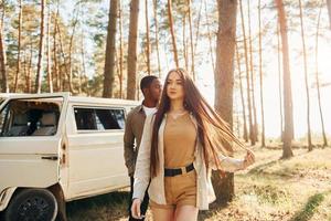 cerca del autobús blanco. una pareja joven viaja juntos por el bosque durante el día foto