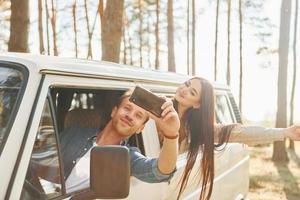 Making selfie. Young couple is traveling in the forest at daytime together photo