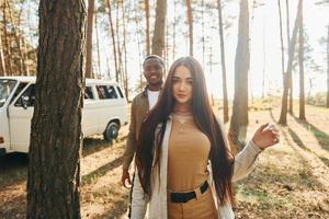 Bus is behind. Young couple is traveling in the forest at daytime together photo