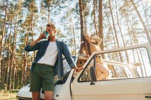 Standing near bus. Young couple is traveling in the forest at daytime together photo