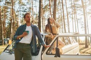 Standing near bus. Young couple is traveling in the forest at daytime together photo