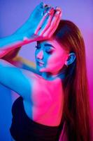 Posing with hands up. Fashionable young woman standing in the studio with neon light photo