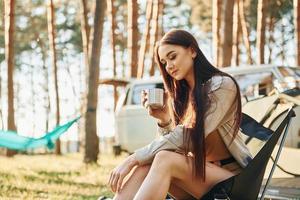 Takes a break and drinking out of cup. Woman is traveling alone in the forest at daytime photo