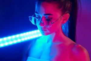 Holds neon lighting stick. Fashionable young woman standing in the studio photo