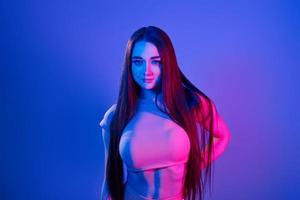 Long brown colored hair. Fashionable young woman standing in the studio with neon light photo