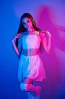 In skirt. Fashionable young woman standing in the studio with neon light photo