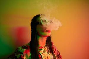 Smoking, activity. Fashionable young woman standing in the studio with neon light photo