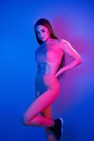 Slim body. Fashionable young woman standing in the studio with neon light photo