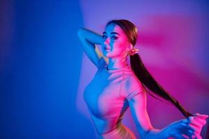 Long brown colored hair. Fashionable young woman standing in the studio with neon light photo