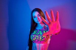 Stop, gesture. Fashionable young woman standing in the studio with neon light photo