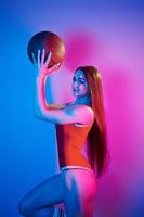 Holds ball. Fashionable young woman standing in the studio with neon light photo