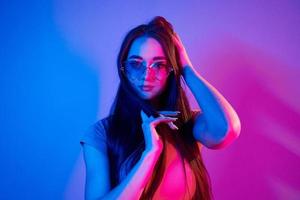 Long brown colored hair. Fashionable young woman standing in the studio with neon light photo