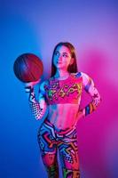 In colorful clothes. Fashionable young woman standing in the studio with neon light photo