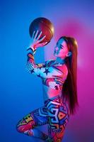 In colorful clothes. Fashionable young woman standing in the studio with neon light photo