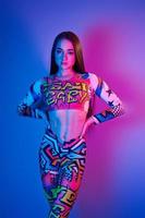 Confident woman in colorful clothes standing in the studio with neon light photo