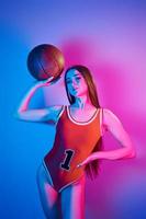 sostiene la pelota. joven de moda parada en el estudio con luz de neón foto