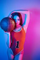 In basketball uniform. Fashionable young woman standing in the studio with neon light photo