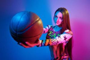 In colorful clothes. Fashionable young woman standing in the studio with neon light photo