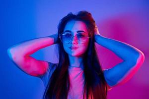 Long brown colored hair. Fashionable young woman standing in the studio with neon light photo