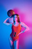 Holds ball. Fashionable young woman standing in the studio with neon light photo