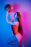 Holds ball. Fashionable young woman standing in the studio with neon light photo