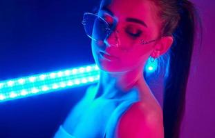 Holds neon lighting stick. Fashionable young woman standing in the studio photo