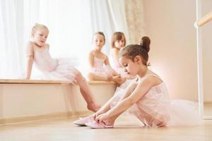 Girl sits on the floor. Little ballerinas preparing for performance by practicing dance moves photo