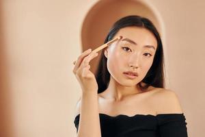 Make up brush. Young serious asian woman standing indoors photo