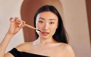 Holds toothbrush. Young serious asian woman standing indoors photo