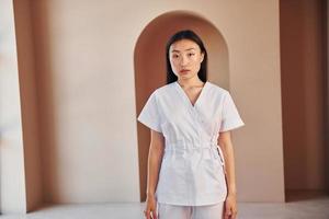 Young female doctor in white coat standing indoors photo