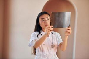 Examining x-ray. Young serious asian woman standing indoors photo