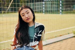 Against net of sport field. Young asian woman is outdoors at daytime photo