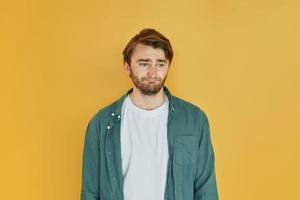 Young man in casual clothes standing indoors in the studio and demonstrates emotions photo