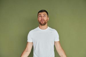 Standing against green background. Young man in casual clothes indoors in the studio photo