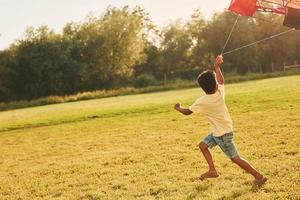 Playing with kite. African american kid have fun in the field at summer daytime photo