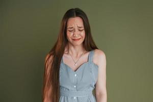 Young woman in casual clothes is crying while standing indoors in the studio photo